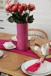 Photo of Color accent table setting. Plates, cutlery, pink napkin and vase with beautiful roses in dining room