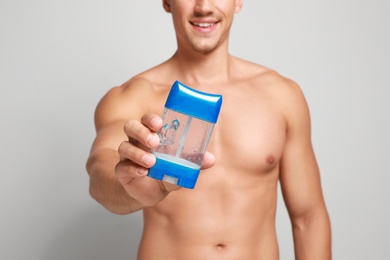 Photo of Young man with deodorant on light background, closeup
