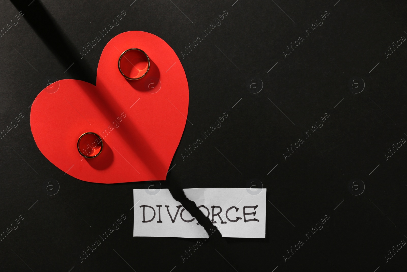 Photo of Pieces of torn card with word Divorce, wedding rings and red paper heart on black background, flat lay. Space for text