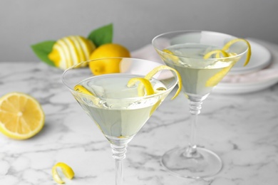 Photo of Glasses of lemon drop martini cocktail with zest on marble table against grey background