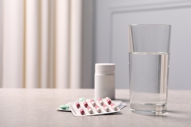 Photo of Different pills in blisters, medical bottle and glass of water on grey table. Space for text