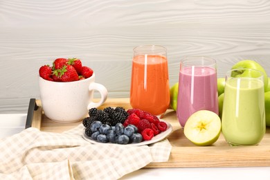 Photo of Glasses of different tasty smoothies and fresh ingredients on white wooden table