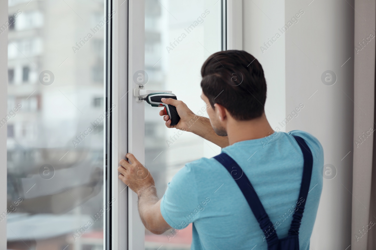 Photo of Construction worker repairing plastic window with electric screwdriver indoors