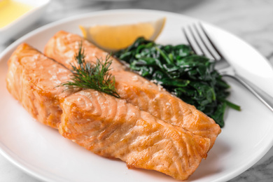 Photo of Tasty salmon with spinach and lemon on plate, closeup