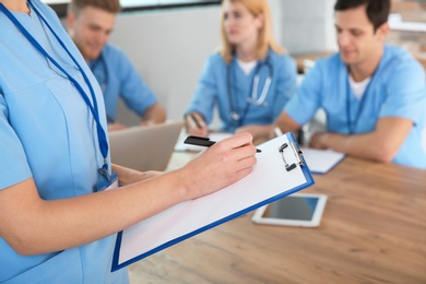 Photo of Medical student with clipboard and her groupmates studying in university library, closeup