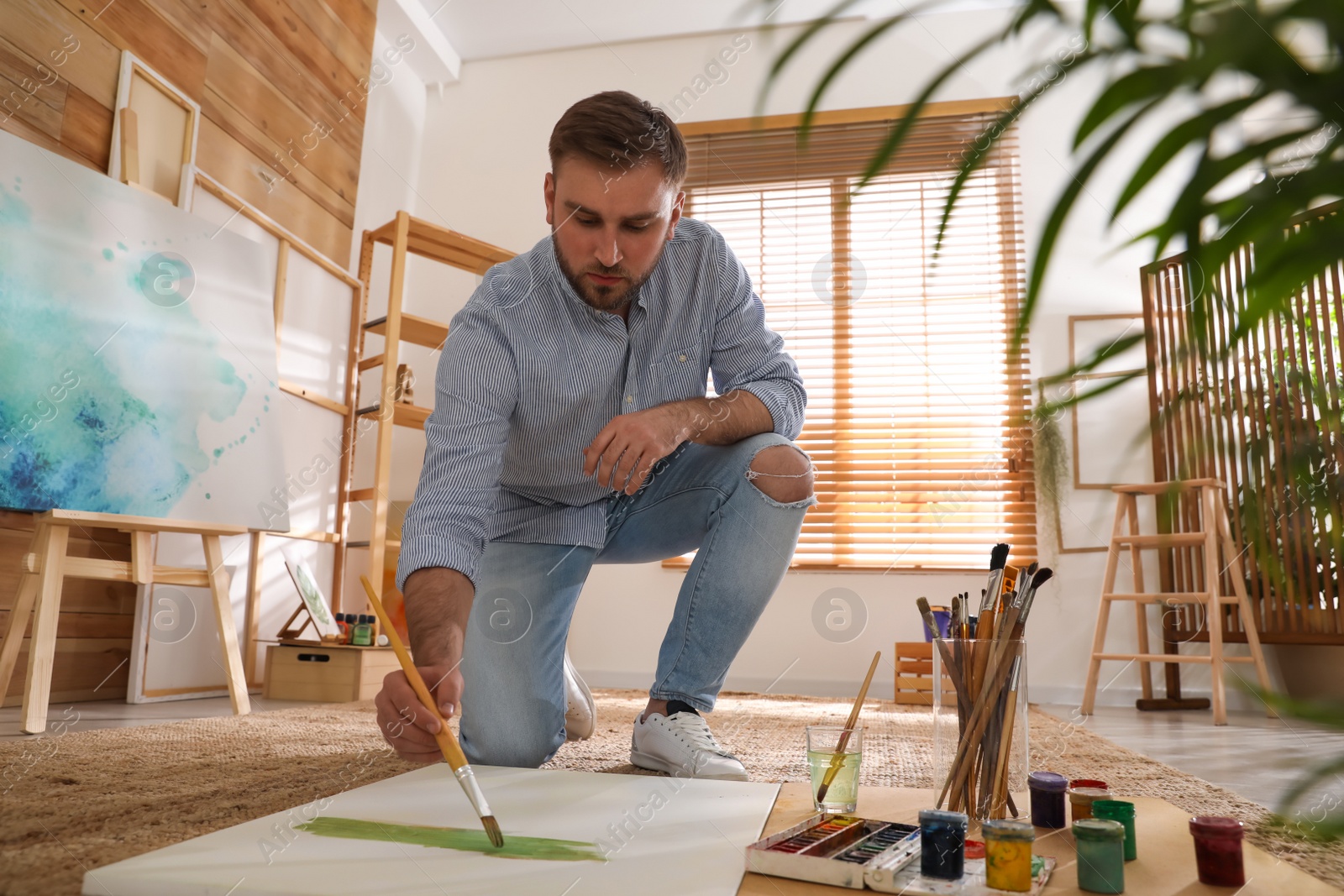 Photo of Young man painting with brush in artist studio