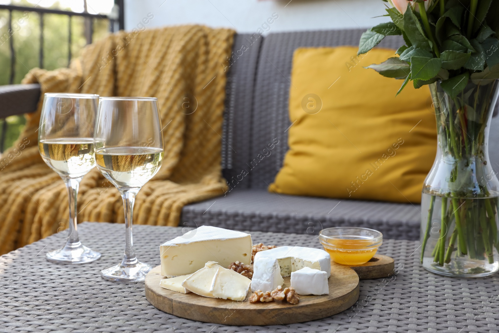 Photo of Vase with roses, glasses of wine and snacks on rattan table at balcony