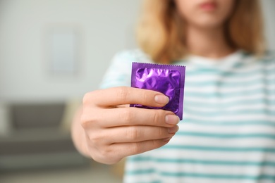Photo of Woman holding condom indoors, closeup. Safe sex concept