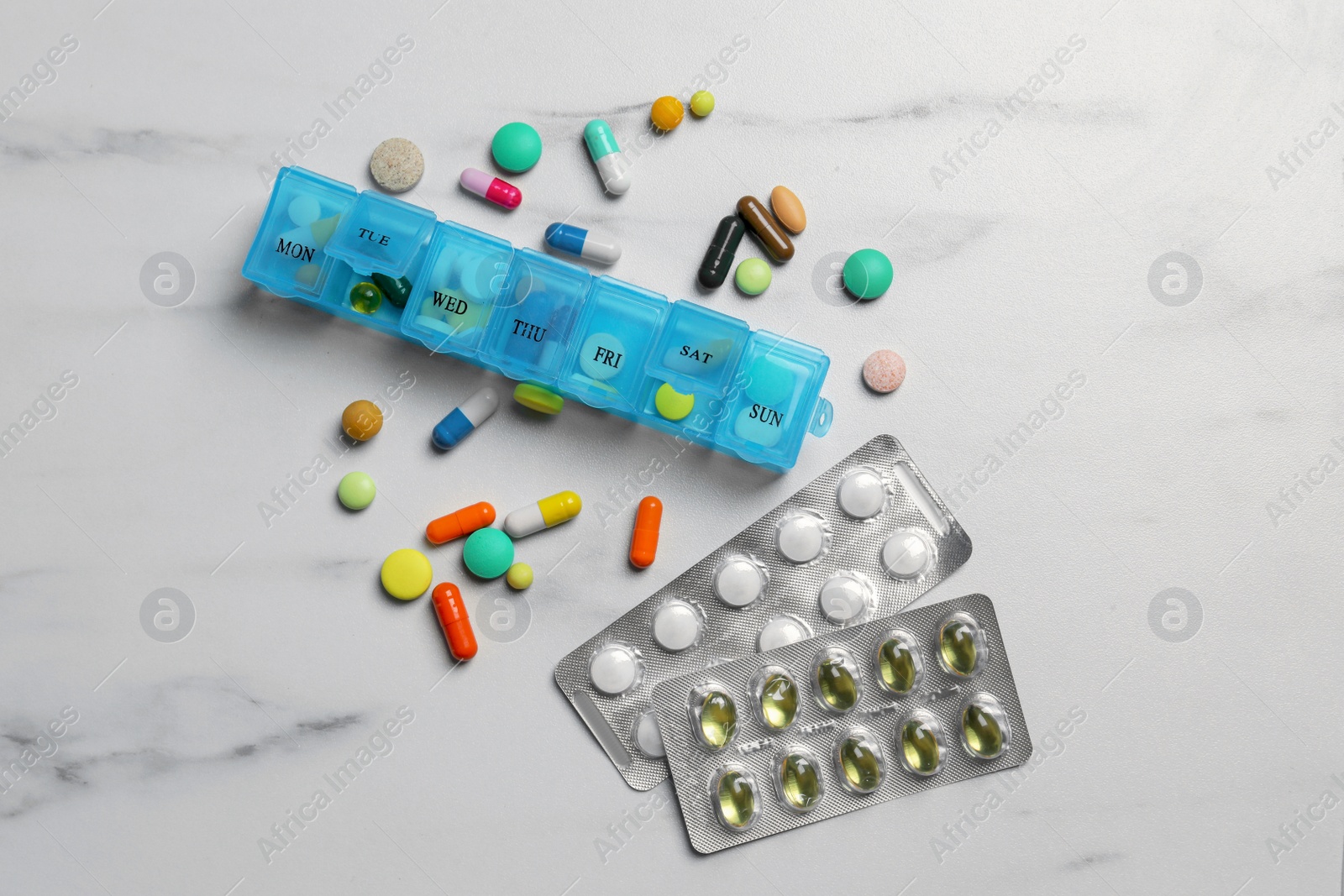 Photo of Weekly pill box with medicaments on white marble table, flat lay