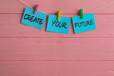 Photo of Paper notes with motivational phrase Create Your Future hanging on pink wooden wall. Space for text