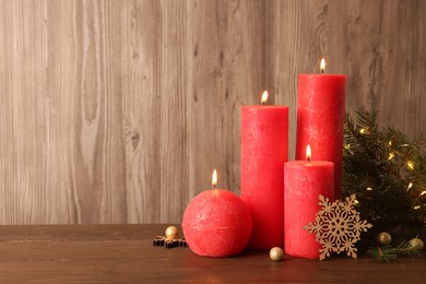 Beautiful burning candles with Christmas decor on wooden table, space for text