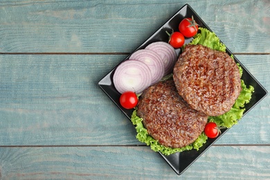 Photo of Grilled meat cutlets for burger on blue wooden table, top view. Space for text