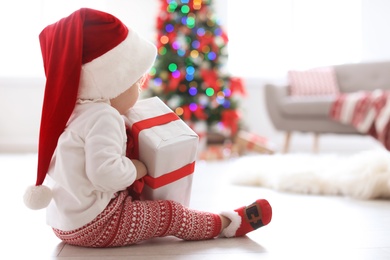 Cute baby in Santa hat with Christmas gift at home