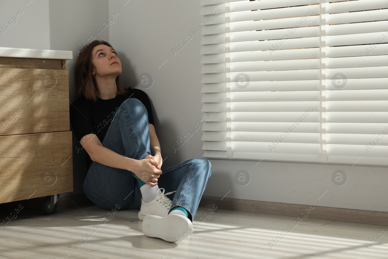 Photo of Sad young woman sitting on floor indoors, space for text