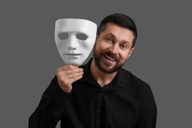 Photo of Multiple personality concept. Happy man with mask on grey background