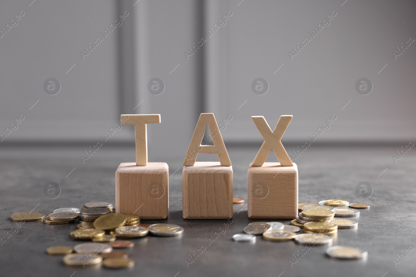 Photo of Word Tax, wooden letters and coins on grey table