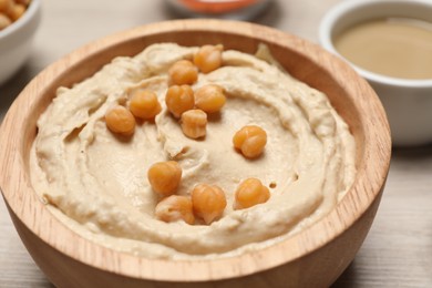 Bowl with delicious hummus and chickpeas on light wooden table, closeup