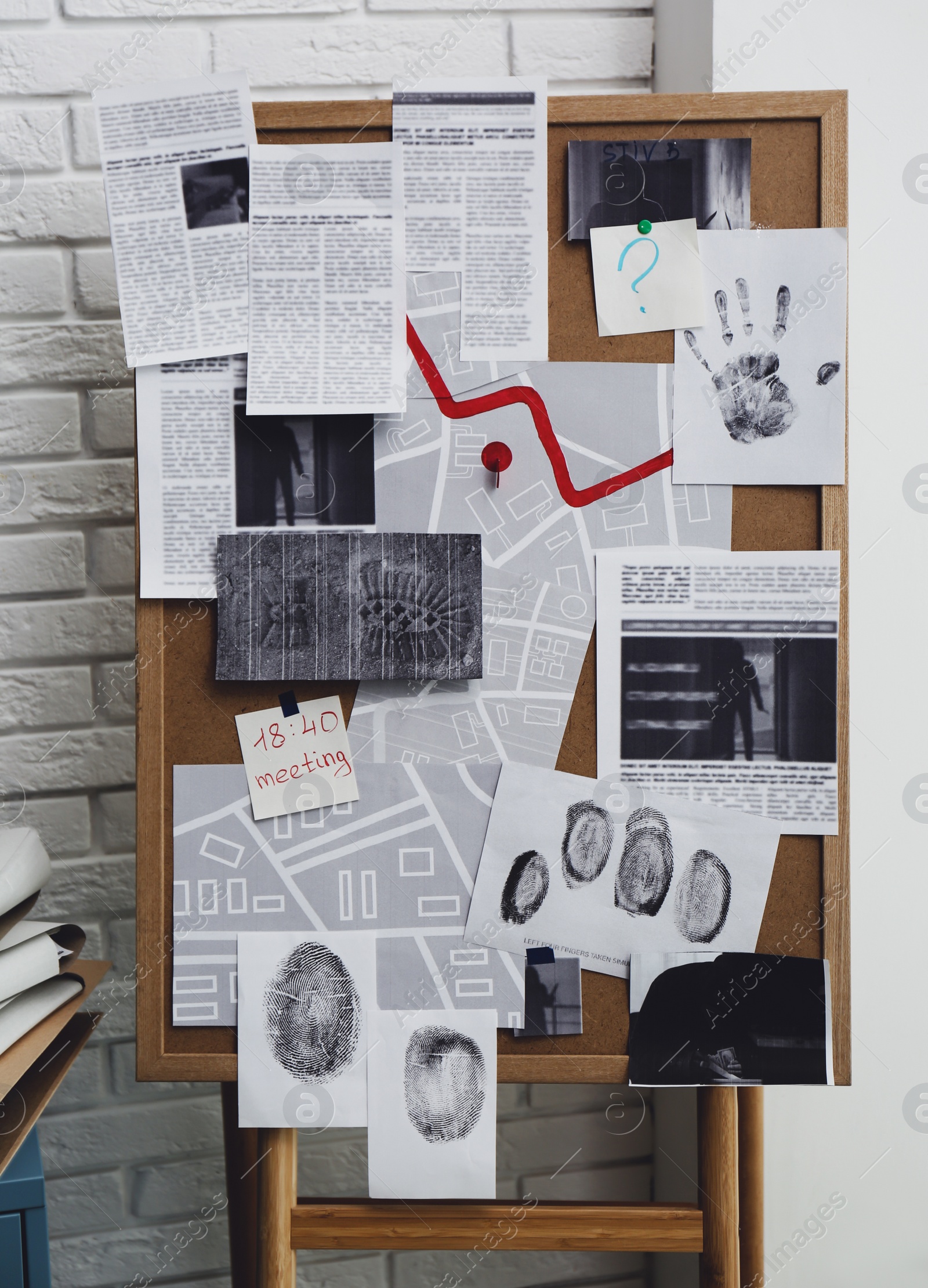 Photo of Detective board with fingerprints, crime scene photos and map near white brick wall indoors