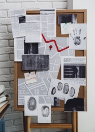 Detective board with fingerprints, crime scene photos and map near white brick wall indoors