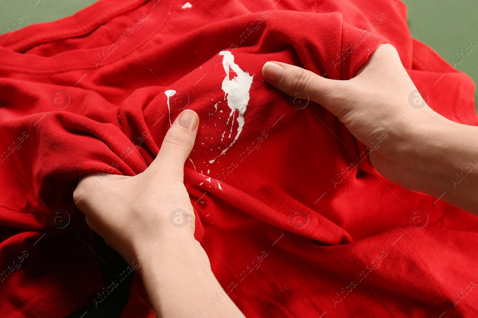 Photo of Woman holding red shirt with white paint stain on green background, closeup