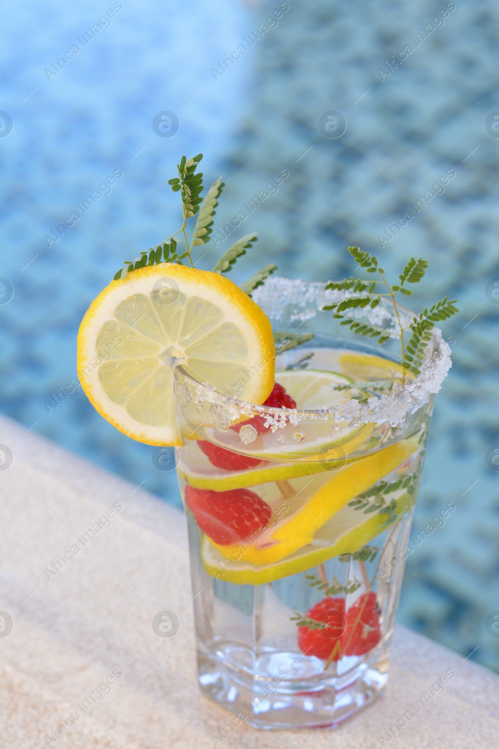 Photo of Delicious refreshing lemonade with raspberries near swimming pool