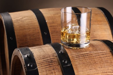 Whiskey with ice cubes in glass on wooden barrel, closeup