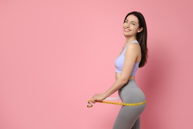 Photo of Happy young woman with measuring tape showing her slim body on pink background, space for text