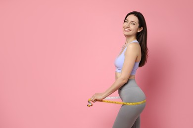 Happy young woman with measuring tape showing her slim body on pink background, space for text