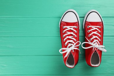 Photo of Pair of red sneakers on turquoise wooden table, flat lay. Space for text