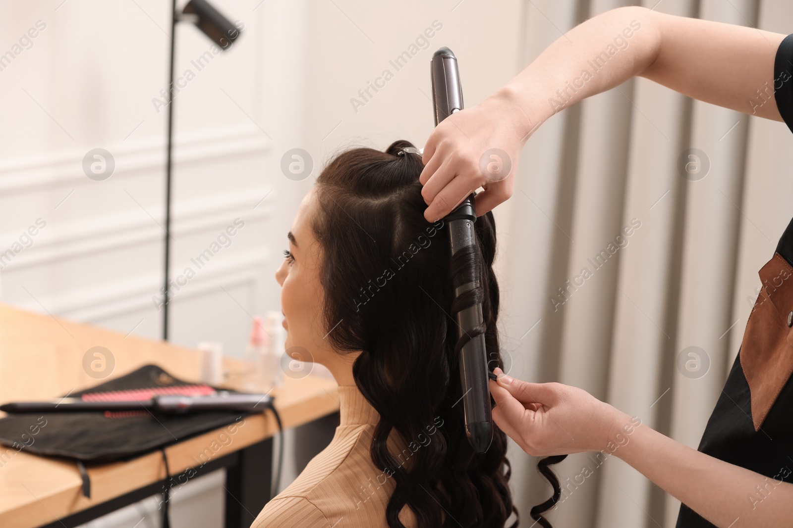 Photo of Hair styling. Hairdresser curling woman's hair in salon, closeup