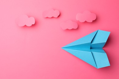 Photo of Handmade light blue paper plane with clouds on pink background, flat lay. Space for text