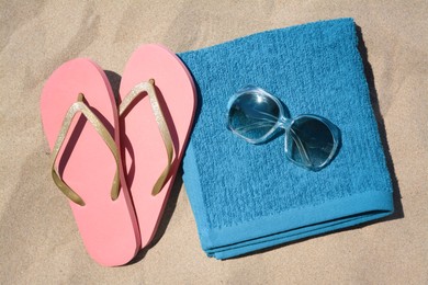 Photo of Folded soft blue beach towel with flip flops and sunglasses on sand, flat lay