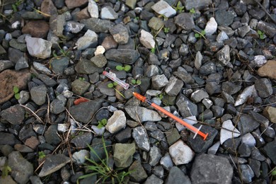 Photo of Disposable syringe with needle on heap of stones outdoors