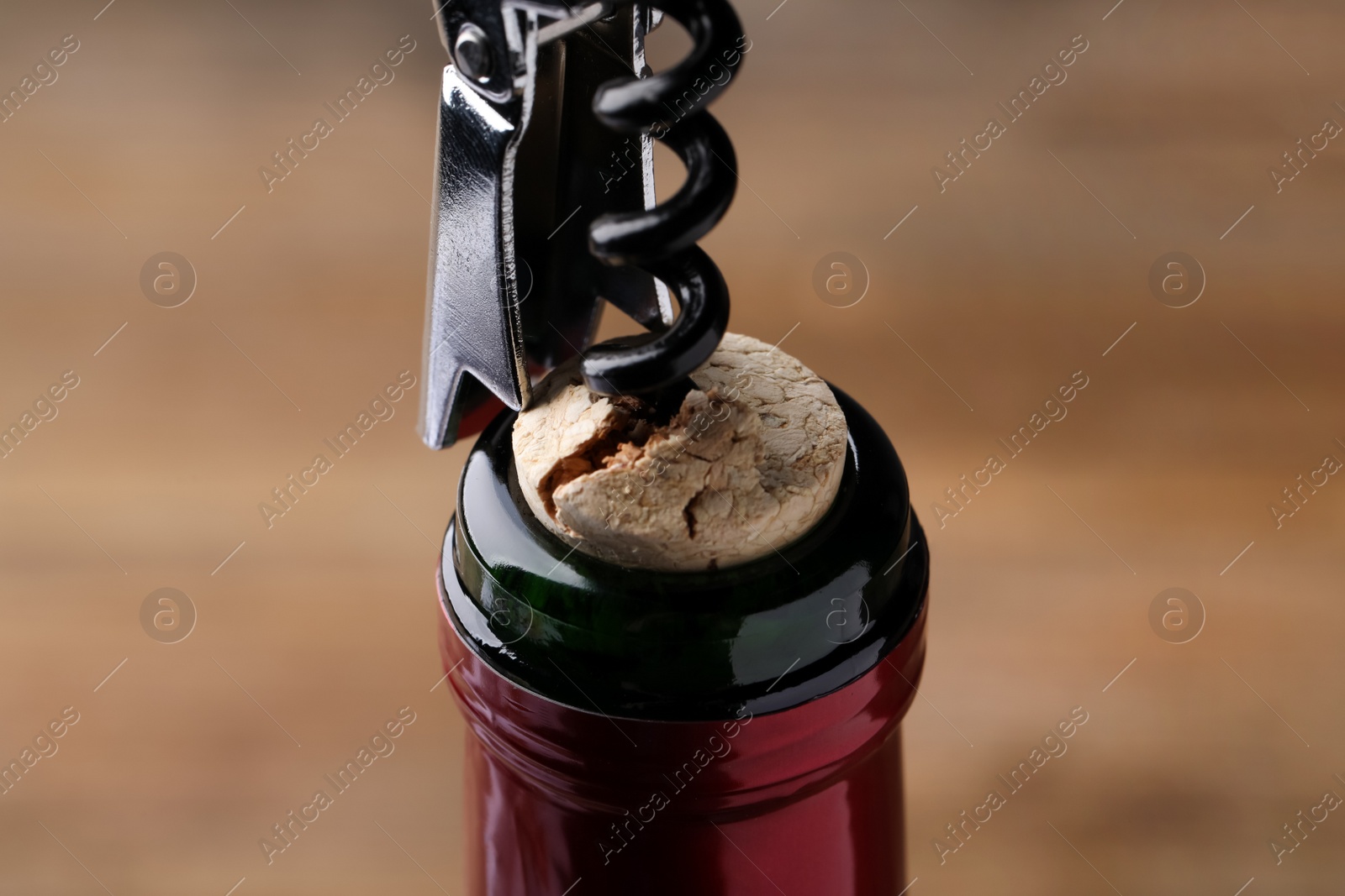 Photo of Opening wine bottle with corkscrew on blurred background, closeup