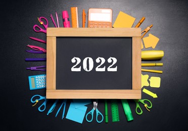 Image of Back to school 2022. Flat lay composition with school stationery and chalkboard on black background