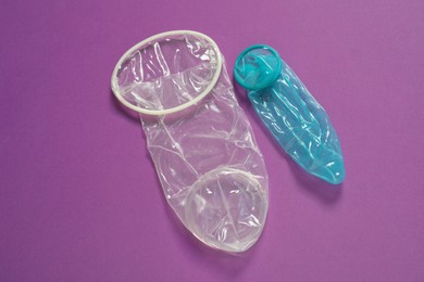 Photo of Unrolled female and male condoms on violet background, above view. Safe sex