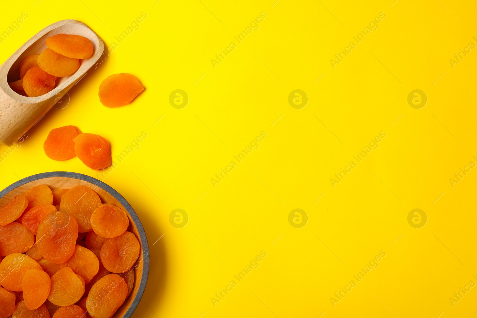 Photo of Bowl and scoop of dried apricots on color background, top view with space for text. Healthy fruit