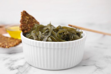 Photo of Tasty seaweed salad in bowl served on white marble table, closeup