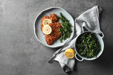 Photo of Tasty schnitzels served with lemon and green beans on grey table, flat lay. Space for text