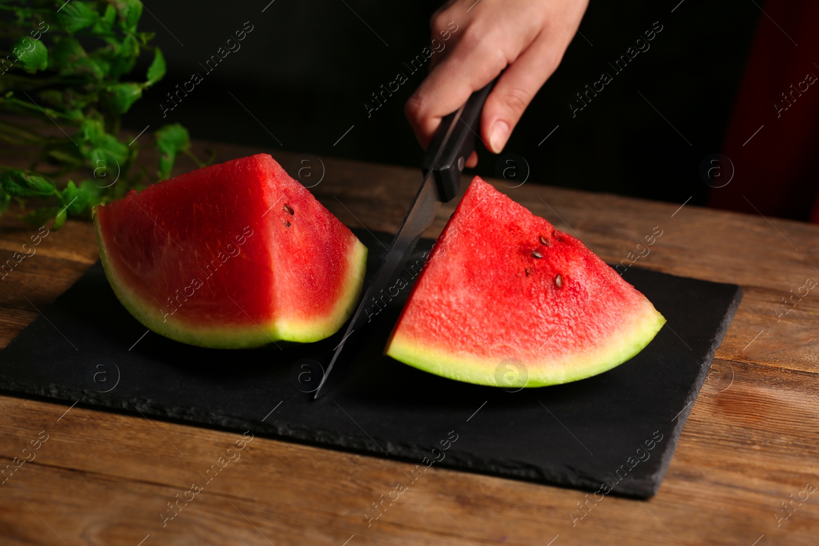 Photo of Woman cutting delicious watermelon on slate board at wooden table, closeup