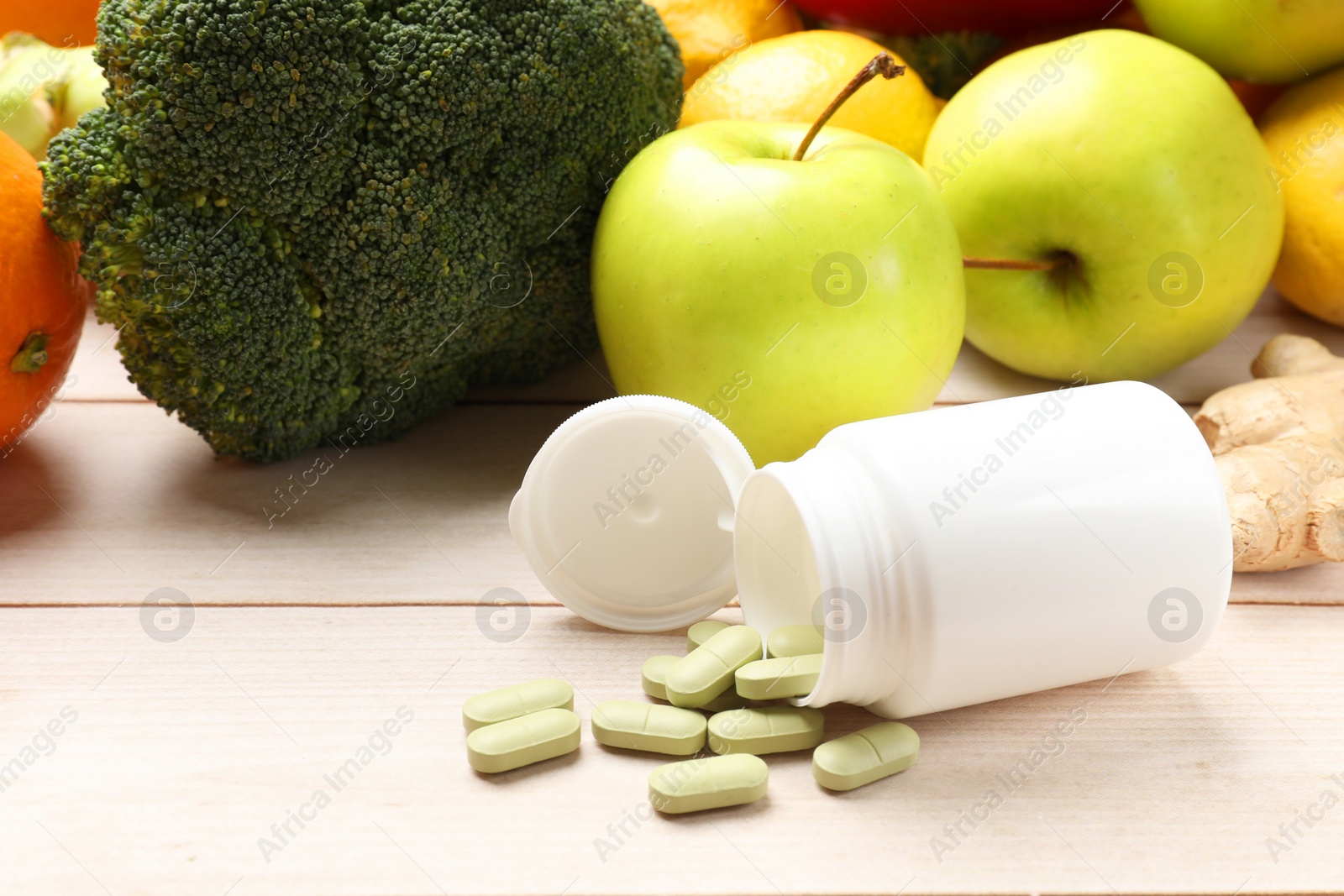 Photo of Dietary supplements. Overturned bottle with pills near food products on light wooden table