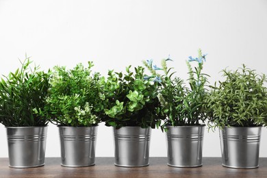 Different artificial potted herbs on wooden table against white background