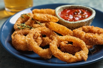 Photo of Homemade crunchy fried onion rings and tomato sauce on plate, closeup