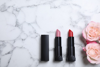Photo of Different lipsticks and beautiful flowers on white marble table, flat lay. Space for text