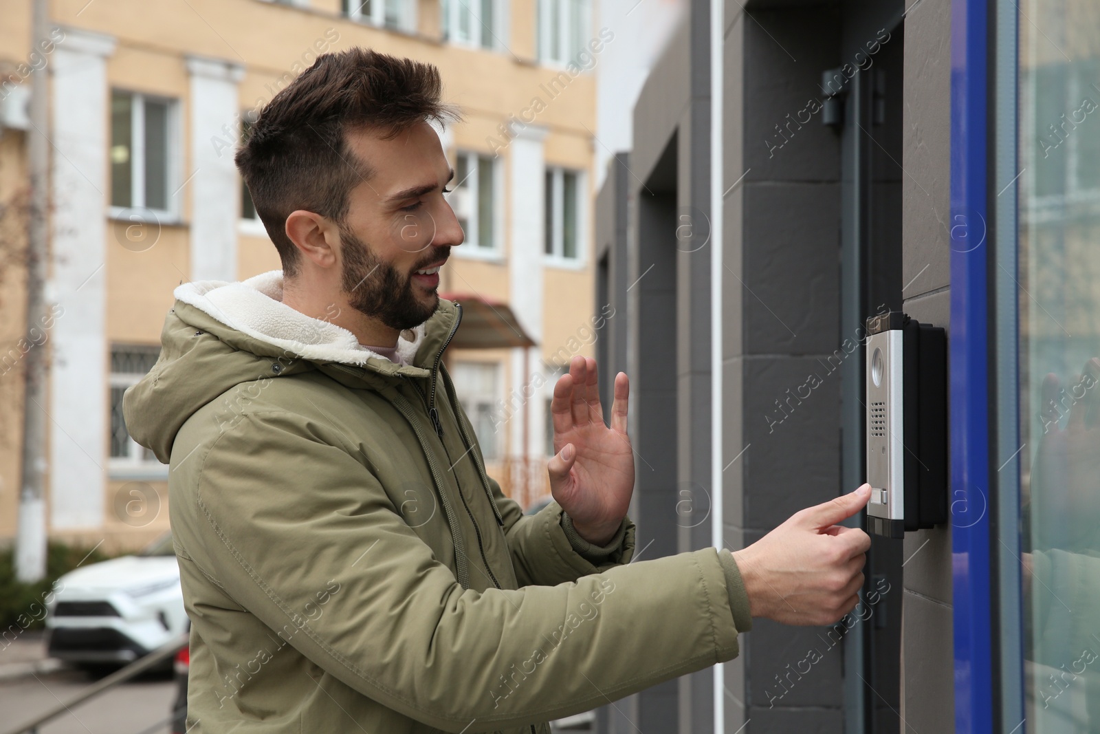 Photo of Happy man ringing intercom while waving to camera near building entrance