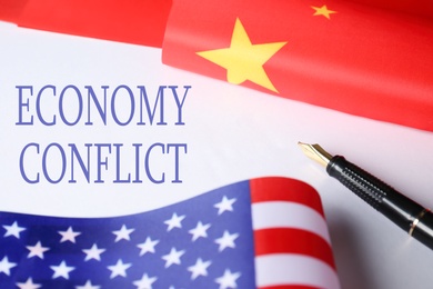 Photo of USA and China flags, pen on paper with text ECONOMY CONFLICT, closeup