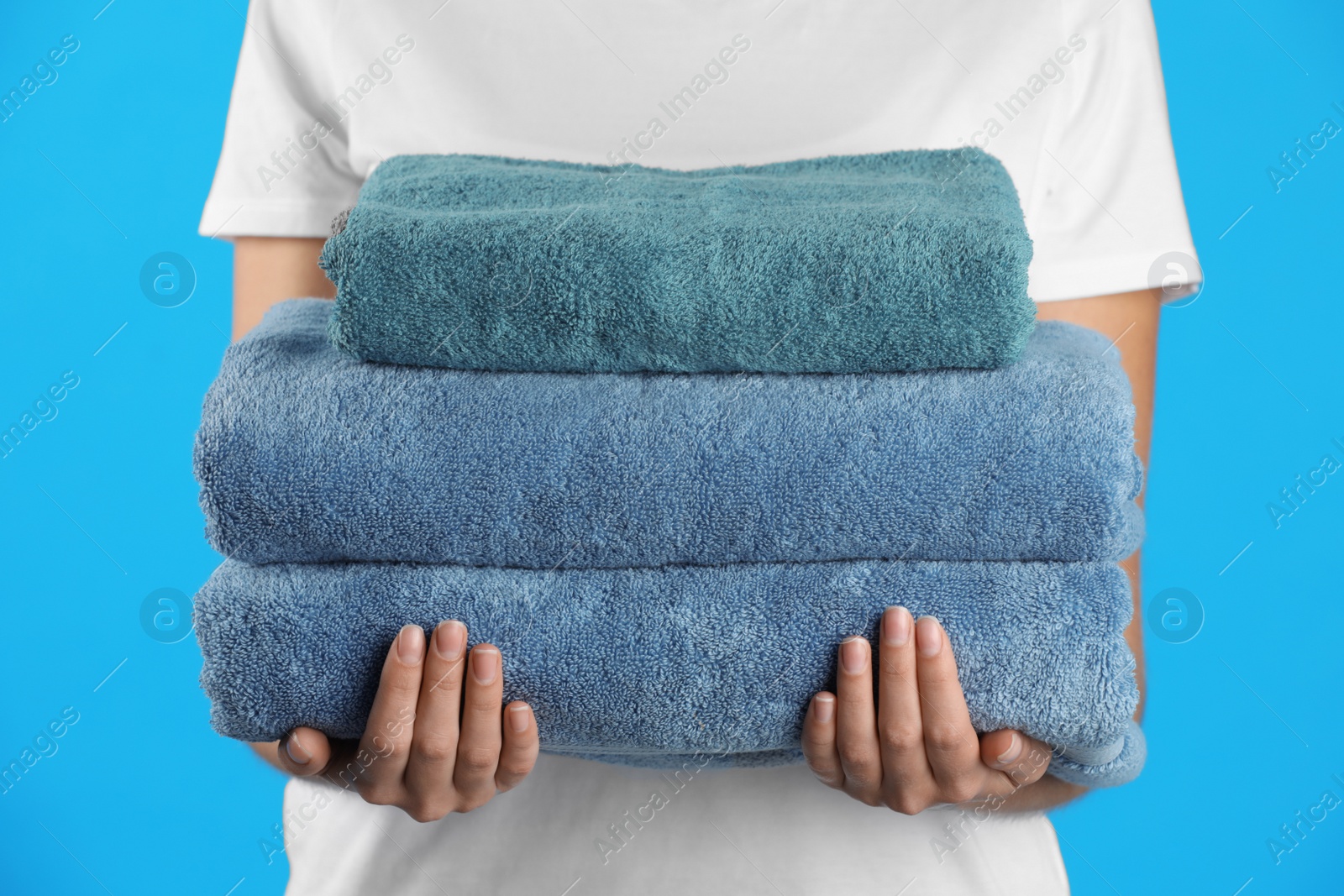 Photo of Woman holding fresh towels on light blue background, closeup