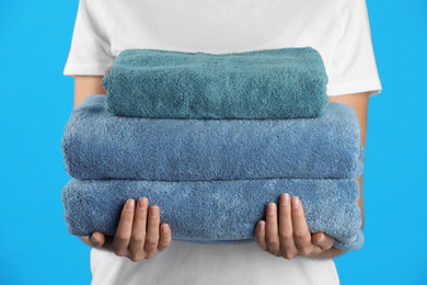 Photo of Woman holding fresh towels on light blue background, closeup