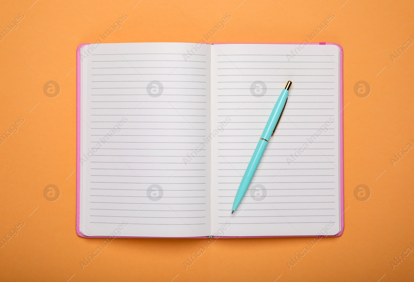 Photo of Open office notebook and pen on pale orange background, top view