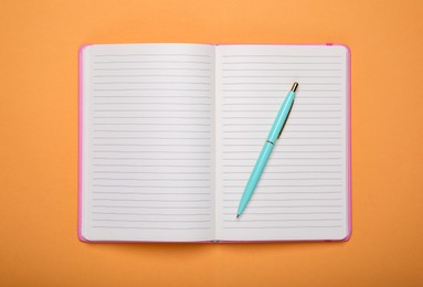 Photo of Open office notebook and pen on pale orange background, top view